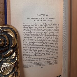 May include: A book page with text from Chapter VI, titled "The Serpent, Son of the Morning and Fall of the Angels." The text discusses angelology and related subjects. The book has a decorative gold edge.