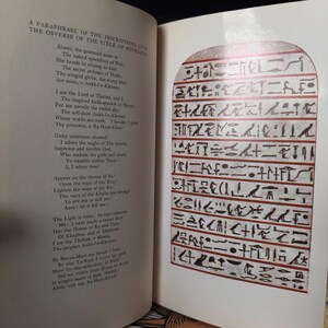 May include: An open book with text and an illustration of ancient Egyptian hieroglyphs. The left page contains a poem titled "A Paraphrase of the Inscriptions Upon the Obverse of the Stele of Revealing." The right page features a detailed illustration of hieroglyphs.