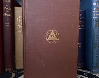 May include: A burgundy hardcover book with a gold emblem on the front cover. The emblem is a triangle with a circle around it. The circle contains a compass, a square, and a letter 'G'. The text 'TRY' is below the emblem.