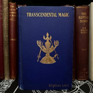 May include: A blue hardback book titled "Transcendental Magic" by Eliphas Levi. The book cover features a gold illustration of a candelabrum with a star and a figure in the centre.