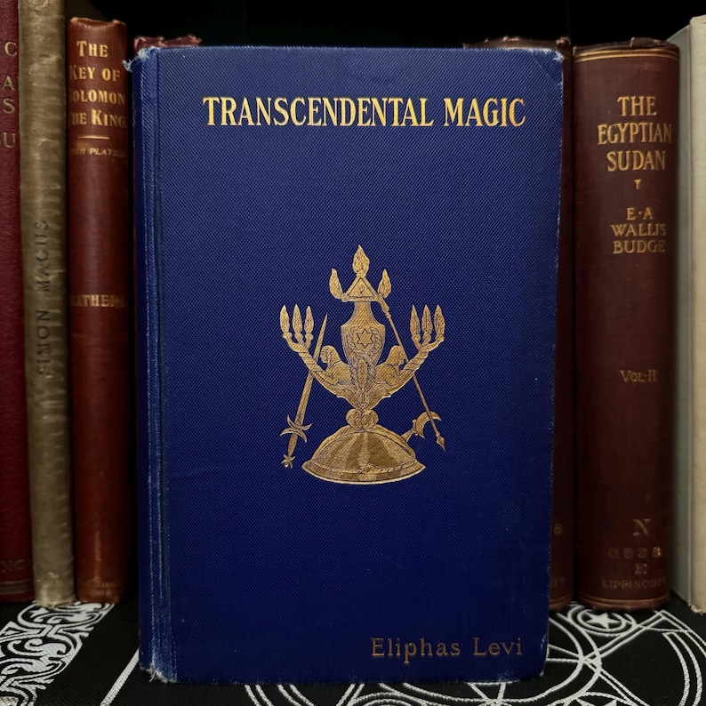 May include: A blue hardback book titled "Transcendental Magic" by Eliphas Levi. The book cover features a gold illustration of a candelabrum with a star and a figure in the centre.