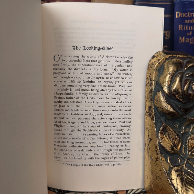Pu&ograve; includere: Un primo piano di una pagina di libro con il titolo "The Looking-Glass" e testo sulle opere di Aleister Crowley. Il testo tratta della diversit&agrave; del suo genio e dell'abbondanza della sua forma. La pagina &egrave; ingiallita dal tempo e ha un aspetto usurato e vintage.
