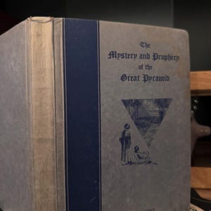 May include: A vintage book titled "The Mystery and Prophecy of the Great Pyramid" with a blue spine and a drawing of two figures standing in front of a pyramid on the cover.