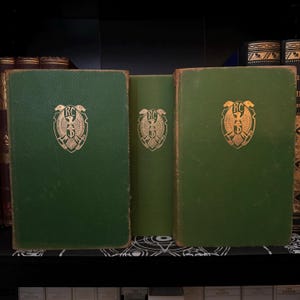 Könnte beinhalten: Drei grüne Hardcover-Bücher mit goldenen Lettern und einem goldenen Adleremblem auf dem vorderen Umschlag. Die Bücher stehen in einem Regal.