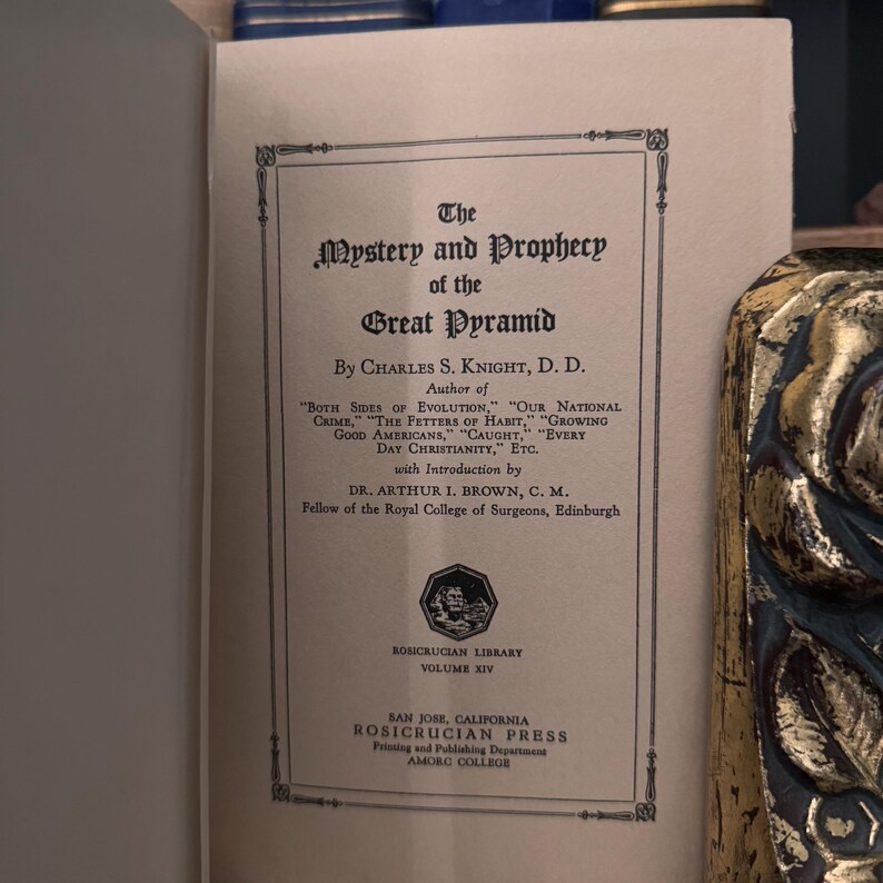 May include: A vintage book cover with the title "The Mystery and Prophecy of the Great Pyramid" by Charles S. Knight, D.D. The book is part of the Rosicrucian Library, Volume XIV. The book was published by the Rosicrucian Press in San Jose, California.