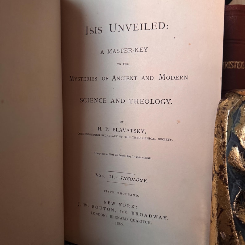 May include: Open book titled "Isis Unveiled" by H.P. Blavatsky. The book's title and author are prominently displayed in black text on a cream-colored page. The book is a master key to the mysteries of ancient and modern science and theology.
