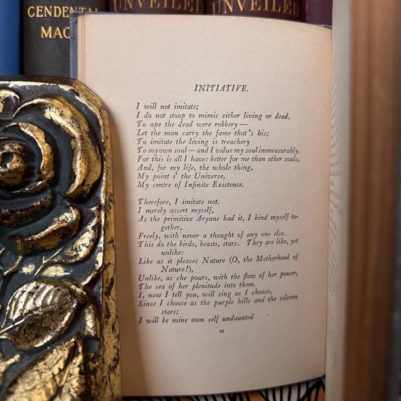 Puede incluir: Un libro abierto con el t&iacute;tulo "INITIATIVE" y un poema impreso en papel envejecido. El libro est&aacute; flanqueado por una cubierta de libro decorativa dorada y negra con un dise&ntilde;o floral. El t&iacute;tulo "UNVEILED" es visible en la parte superior.