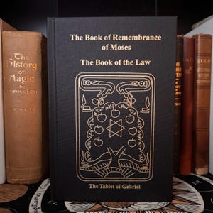 Peut inclure: Un livre noir avec des lettres et des illustrations dor&eacute;es. Le titre est "The Book of Remembrance of Moses" et "The Book of the Law". La couverture pr&eacute;sente un motif d'arbre d&eacute;taill&eacute; avec une &eacute;toile &agrave; six branches et le texte "The Tablet of Gabriel."