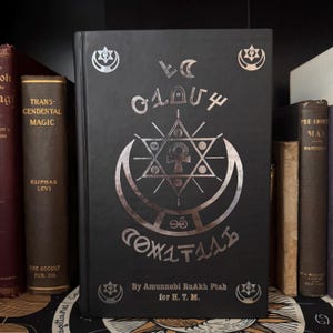 Könnte beinhalten: Ein schwarzes Buch mit silbernen geprägten Symbolen und Text. Das Cover zeigt einen Stern, einen Mond und andere esoterische Designs. Der Titel des Buches ist in einer ungewöhnlichen Schriftart. Der Autor ist Amunnubi RuAkh Ptah.