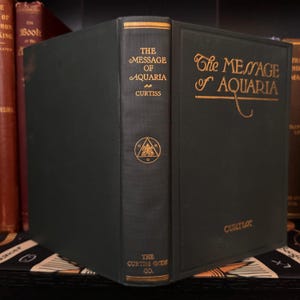 May include: A green hardcover book titled "The Message of Aquaria" by Curtiss. The book features a gold-colored title and a symbol on the spine.