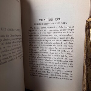 May include: Open book with text on aged paper. The text reads "CHAPTER XVI. RESURRECTION OF THE BODY" and discusses reincarnation. The book is open to a page with printed text, with the title and chapter number visible.