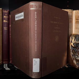 May include: A brown hardcover book titled "BLACK - THE BOOK OF ENOCH OR I ENOCH" with "S.V.T.P. VOL VII" at the top. The spine includes a library label. The book is part of a collection of antique books.