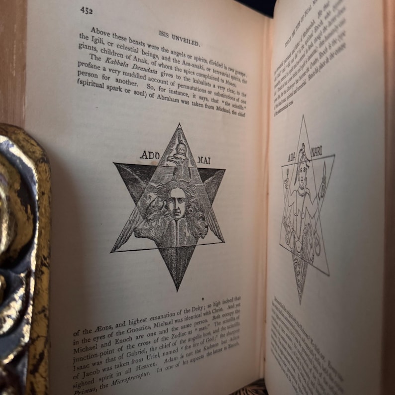 May include: Open book with text and illustrations. Page 452 displays text about angels and spirits, with a star-shaped illustration containing the words "ADO MAI." The opposite page features a similar illustration with the words "ADA MARI."