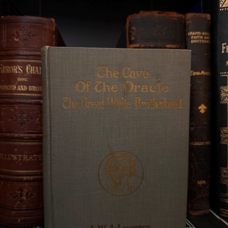 May include: A vintage book titled "The Cave Of The Oracle The Great White Brotherhood" with a gold-coloured illustration of a person's head on the front cover.