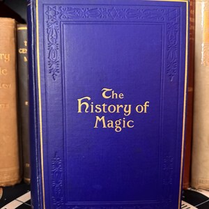 Puede incluir: Un libro de tapa dura azul con letras doradas que dicen "The History of Magic".