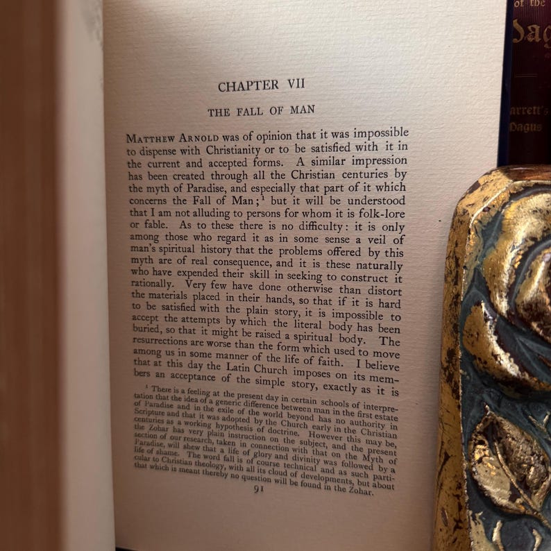 May include: An open book with the title "Chapter VII The Fall of Man" printed on the page. The text is in black ink. A decorative gold and blue book spine is visible on the right. The book appears to be an antique.