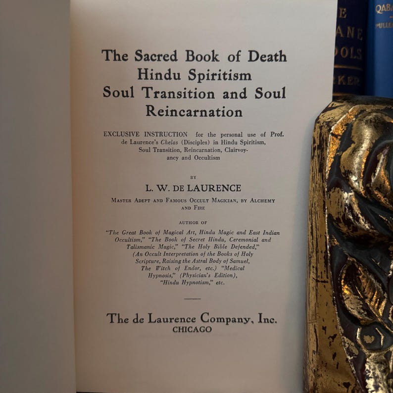 May include: A black and white book titled "The Sacred Book of Death Hindu Spiritism Soul Transition and Soul Reincarnation" by L.W. de Laurence, Master Adept and Famous Occult Magician, by Alchemy and Fire. The book cover also lists the author's other books, including "The Great Book of Magical Art, Hindu Magic and East Indian Occultism", "The Book of Secret Hindu, Ceremonial and Talismanic Magic", "The Holy Bible Defended", "The Witch of Endor", "Medical Hypnosis", and "Hindu Hypnotism".