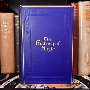 Puede incluir: Un libro de tapa dura azul con letras doradas en el lomo y la portada. El t&iacute;tulo del libro es "The History of Magic".