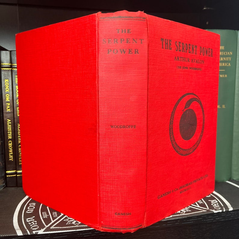 May include: A red hardback book titled "The Serpent Power" by Arthur Avalon (Sir John Woodroffe). The book cover features a black and white illustration of a snake coiled in a circle.