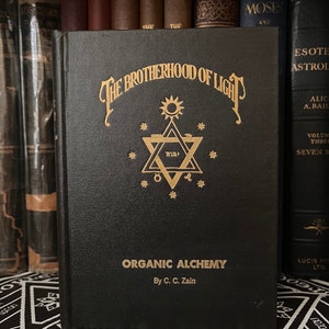 May include: A black book with gold lettering titled "The Brotherhood of Light: Organic Alchemy by C.C. Zain". The cover features a gold star of David with a sun above it.