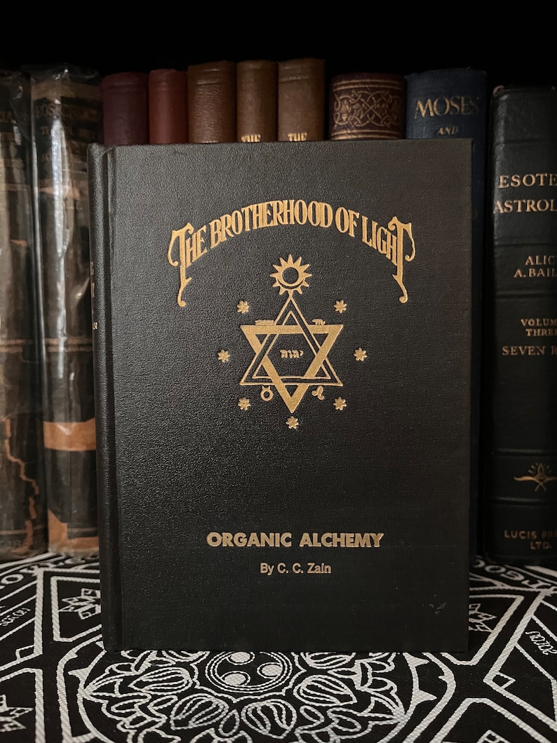 May include: A black book with gold lettering titled "The Brotherhood of Light: Organic Alchemy by C.C. Zain". The cover features a gold star of David with a sun above it.