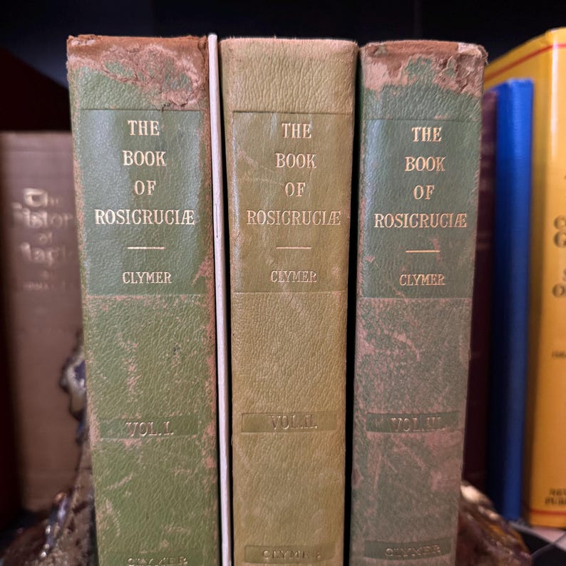 Może przedstawiać: Trzy stare zielone książki z pozłacanymi napisami zatytułowane "The Book of Rosicruciae" autorstwa Clymera. Książki to tomy I, II i III.