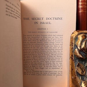 May include: An open book displaying the title "THE SECRET DOCTRINE IN ISRAEL." The text discusses Kabalism and historical figures. The book has a decorative spine, and the pages are aged.