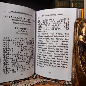 May include: An open book with pages displaying ancient text and symbols. The text is in black ink on aged paper. The book is titled "The Sacred Tablet of Tama-Re" and includes the text "El Neteru The Guardians".