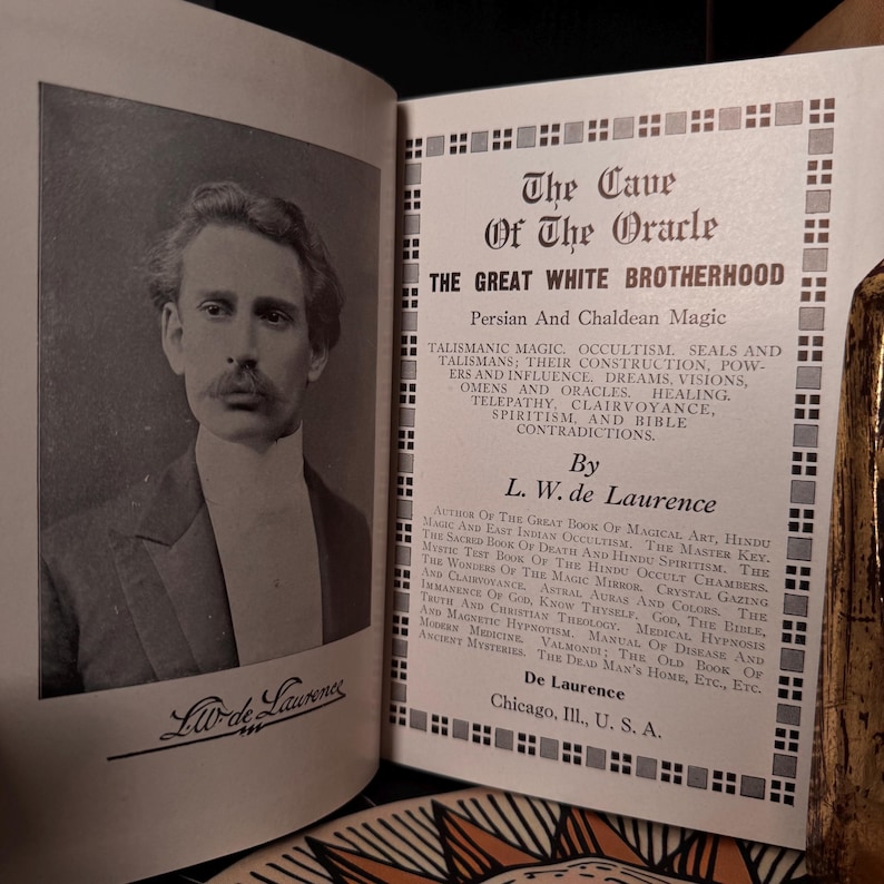 May include: An open book with a black and white portrait of a man on the left page and text on the right page. The text reads "The Cave of the Oracle" and "Persian and Chaldean Magic" by L.W. de Laurence.