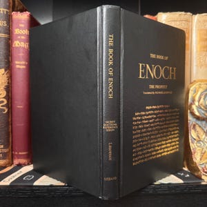 May include: A black hardcover book titled "The Book of Enoch" with gold lettering. The spine reads "The Book of Enoch" and "Secret Doctrine Reference Series." The book is displayed on a shelf with other books.
