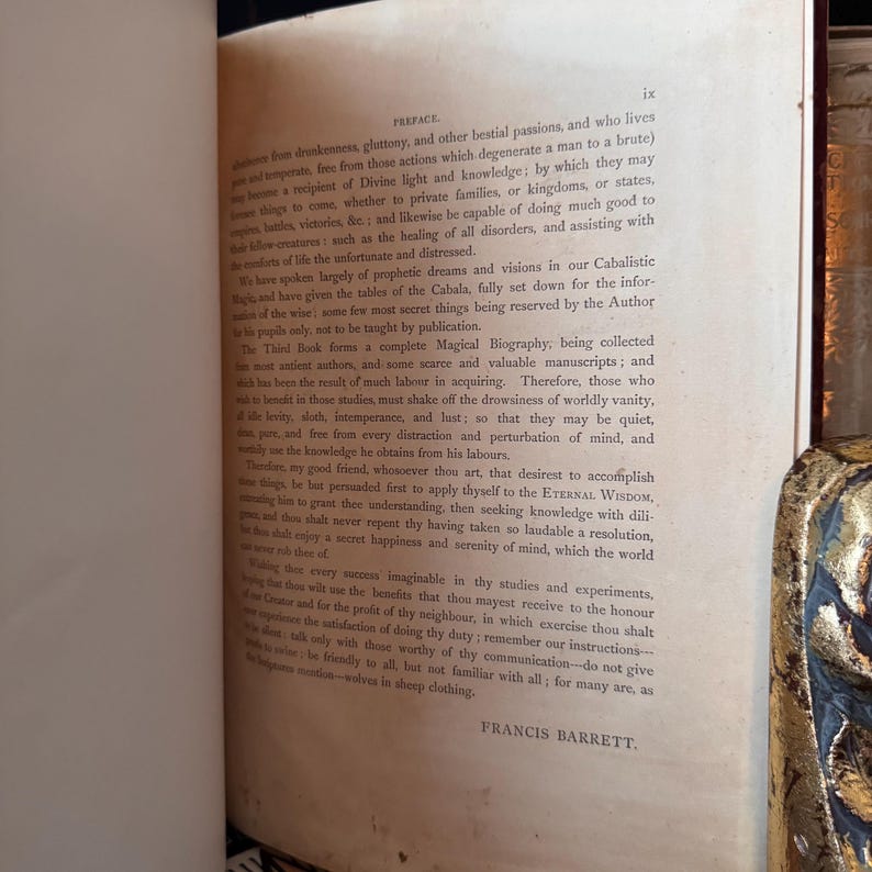 Puede incluir: Libro abierto con texto sobre papel envejecido. La p&aacute;gina muestra el prefacio de un libro, con el nombre del autor, Francis Barrett, en la parte inferior. Las p&aacute;ginas del libro est&aacute;n amarillentas por la edad y el texto es negro.