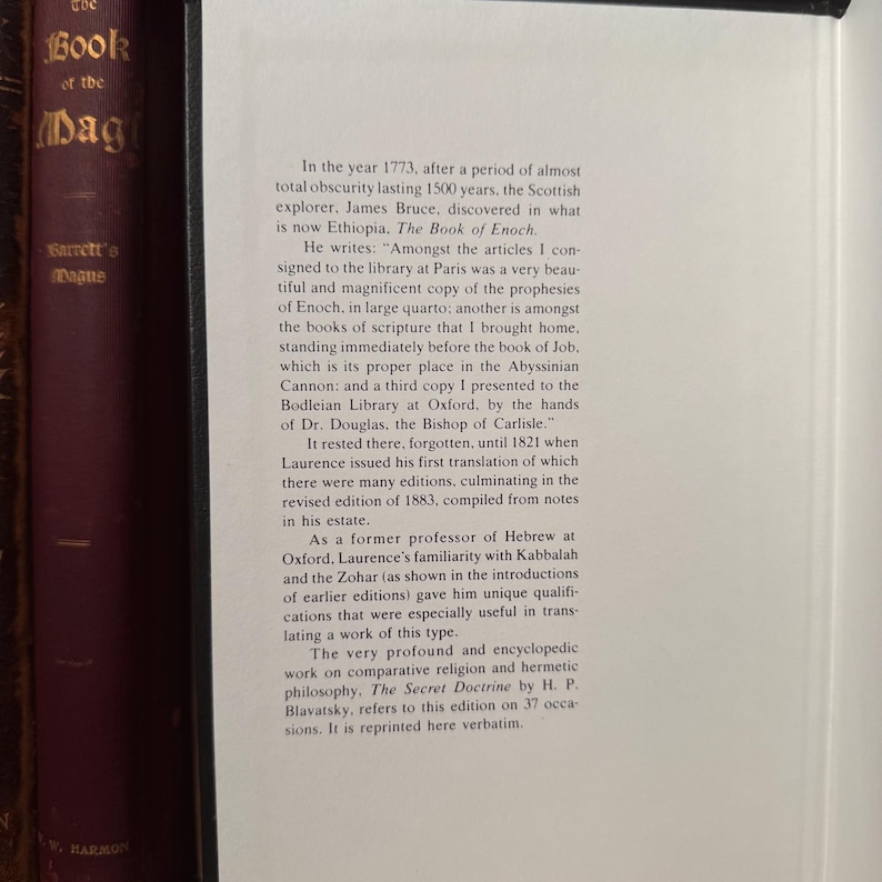 May include: A close-up of a book page with text from "The Book of Enoch" and "The Secret Doctrine" by H.P. Blavatsky. The text is in black font on a cream-colored page. The book is next to other books with dark burgundy covers.