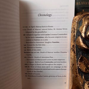 May include: An open book displays a page titled "Chronology" with historical dates and events. The text details the life of Marcus, including his birth, adoption, and death, along with other significant historical events.