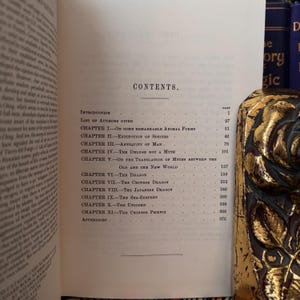 May include: A black and white book titled "Dragons" with a table of contents listing chapters on the dragon, Chinese dragon, Japanese dragon, sea-serpent, unicorn, and Chinese phoenix.