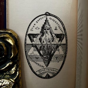 May include: A black and white illustration of a man with a beard and crown, sitting on a triangle with the words "QVOD SVPERIVS" and "MACROPROSO-PUS" written around the top of the triangle. The words "QVOD INFERIVS" and "MICROCOSM" are written around the bottom of the triangle.