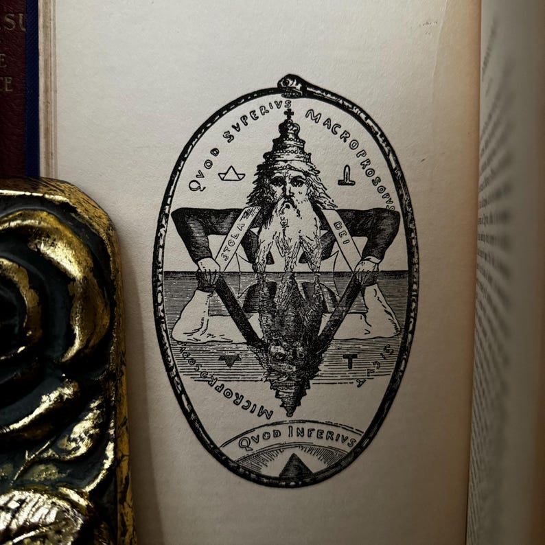 May include: A black and white illustration of a man with a beard and crown, sitting on a triangle with the words "QVOD SVPERIVS" and "MACROPROSO-PUS" written around the top of the triangle. The words "QVOD INFERIVS" and "MICROCOSM" are written around the bottom of the triangle.