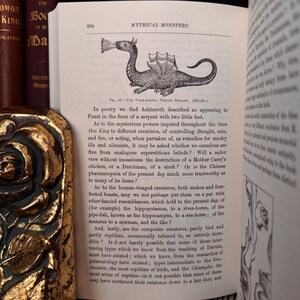 May include: A black and white illustration of a four-legged winged dragon with a long tail. The dragon is breathing fire from its mouth. The illustration is from a book titled "Mythical Monsters". The text below the illustration discusses the mythical creature Ashtaroth, described as a serpent with two little feet.