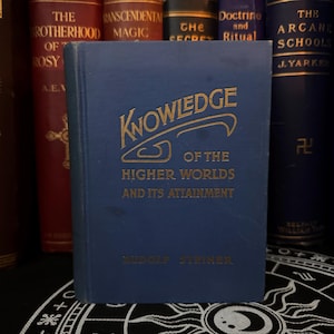 May include: A blue hardcover book with gold lettering titled "Knowledge of the Higher Worlds and Its Attainment" by Rudolf Steiner.