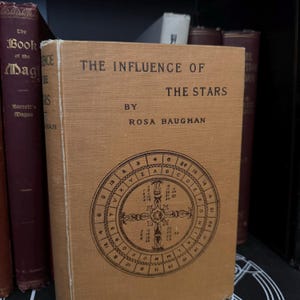 May include: A vintage book titled "The Influence of the Stars" by Rosa Baughan. The book cover is brown with a circular design featuring letters and numbers.