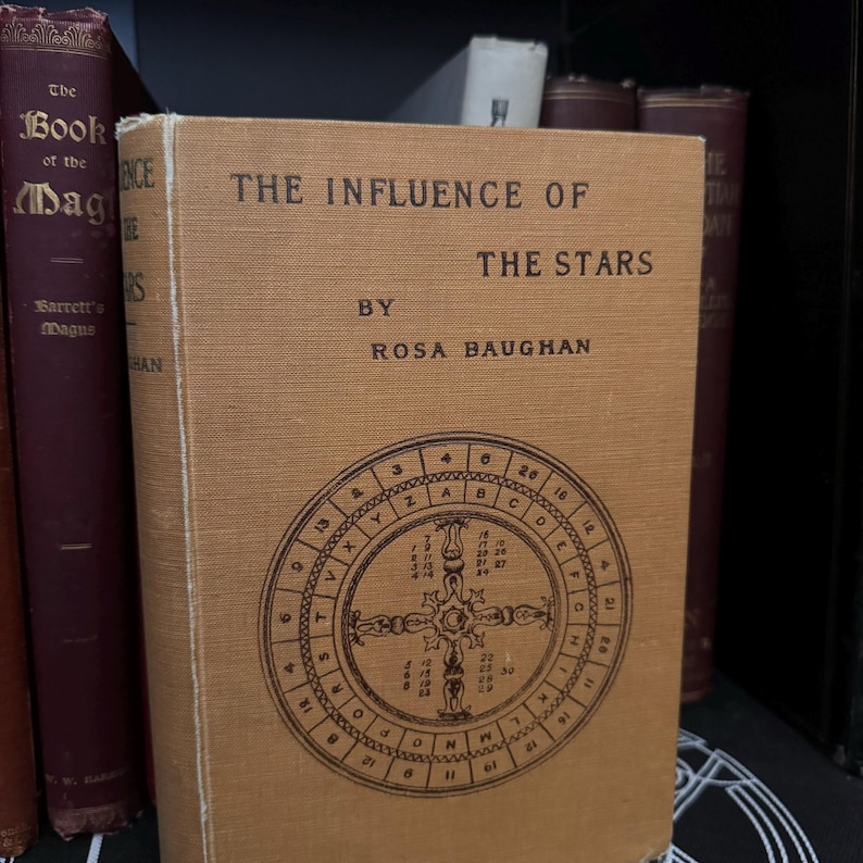 May include: A vintage book titled "The Influence of the Stars" by Rosa Baughan. The book cover is brown with a circular design featuring letters and numbers.
