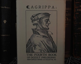 May include: A book titled "AGRIPPA: THE FOURTH BOOK OF OCCULT PHILOSOPHY" with a black and white illustration of a man in a hat. The book is from Heptangle Books, Gillette, NJ. Other books are visible in the background.