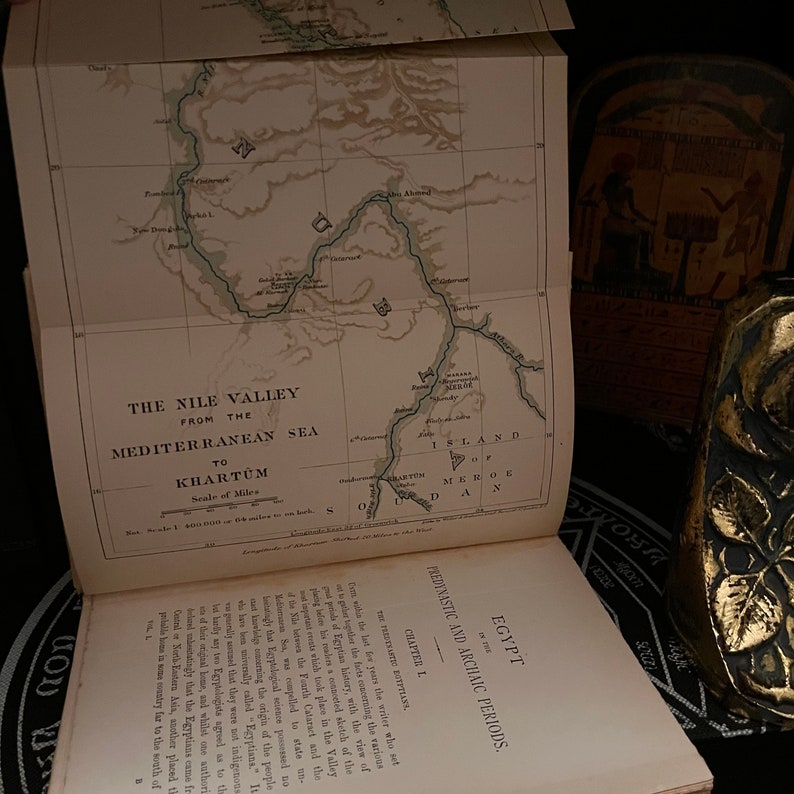 May include: An open book with a map of the Nile Valley from the Mediterranean Sea to Khartoum. The map is in black and white and shows the Nile River winding through the desert. The book is titled "Egypt: Predynastic and Archaic Periods."