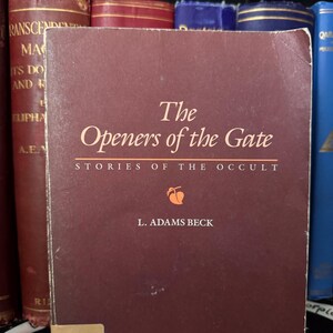 以下が含まれることがあります： L. アダムズ・ベック著「The Openers of the Gate」というタイトルと「Stories of the Occult」というサブタイトルが書かれた、えんじ色のハードカバーの本。本の表紙には、桃色の小さな果物のイラストが描かれている。
