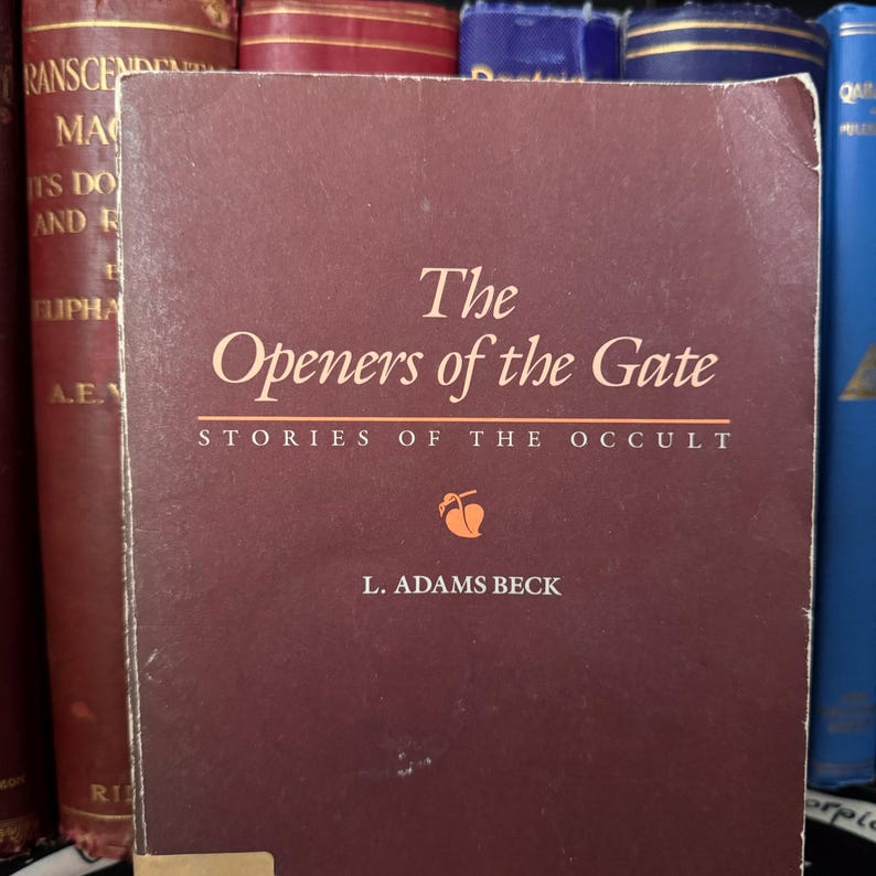 以下が含まれることがあります： L. アダムズ・ベック著「The Openers of the Gate」というタイトルと「Stories of the Occult」というサブタイトルが書かれた、えんじ色のハードカバーの本。本の表紙には、桃色の小さな果物のイラストが描かれている。