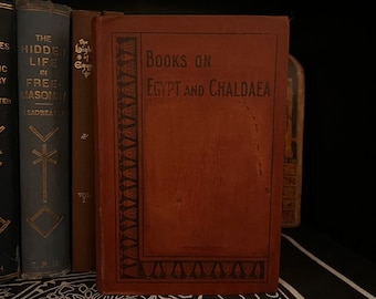 Może przedstawiać: Brązowa książka z tytułem "Books on Egypt and Chaldaea" na okładce. Książka ma ozdobną ramkę z wzorem stylizowanych kwiatów lotosu.