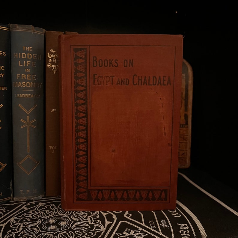 May include: A brown book with the title "Books on Egypt and Chaldaea" on the cover. The book has a decorative border with a pattern of stylized lotus flowers.