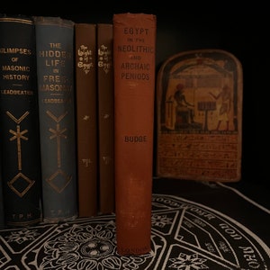 May include: A brown hardcover book titled "Egypt in the Neolithic and Archaic Periods" by E.A. Wallis Budge. The book is on a black surface with a white design.