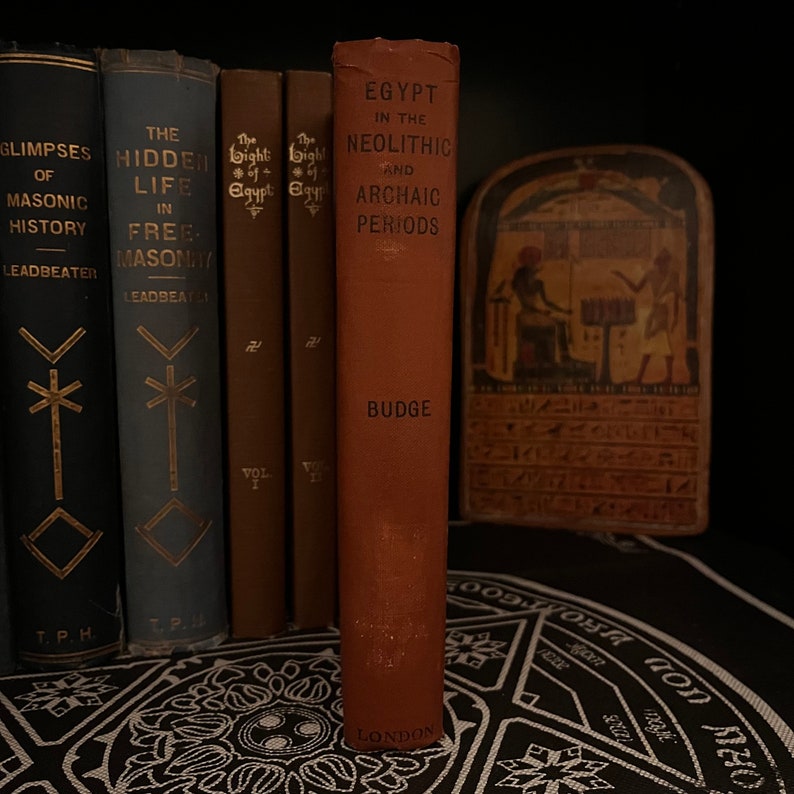 May include: A brown hardcover book titled "Egypt in the Neolithic and Archaic Periods" by E.A. Wallis Budge. The book is on a black surface with a white design.