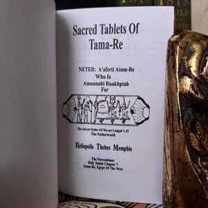 May include: An open book titled "Sacred Tablets Of Tama-Re" is shown. Text includes "NETER: A'aferti Atum-Re", "Amunnubi Ruakhptah", and "The Secret Order Of Wa-set Lodge# 1-19". The book's pages are white, with black text. The book is partially visible.