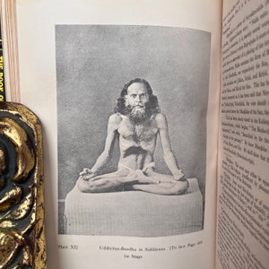 May include: A black and white photograph of a man sitting in a yoga pose. The man is wearing a loincloth and has a long beard. The photo is from a book titled "The Book of Yoga" and the caption reads "Uddiyana-Bandha in Siddhasana 1st Stage".